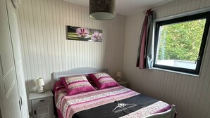 Una camera da letto con un letto, un comodino, una lampada, una finestra con tende e un quadro appeso al muro.