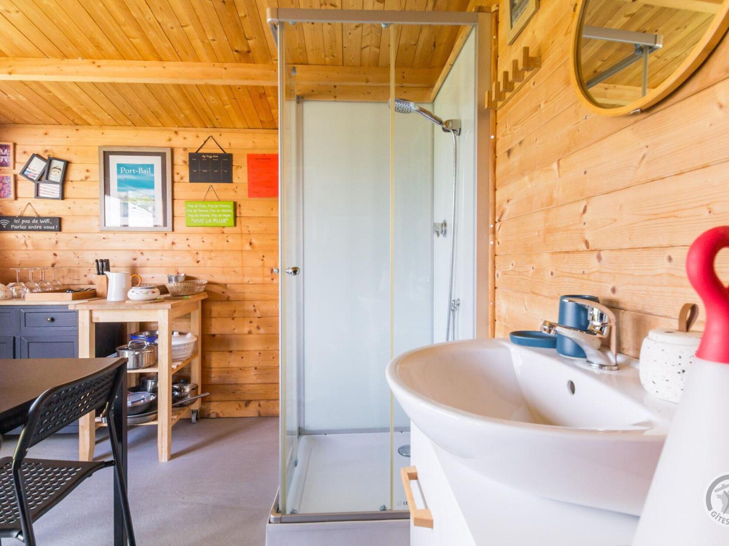 A wooden cabin interior with a kitchenette, a shower area, and a dining table with chairs.