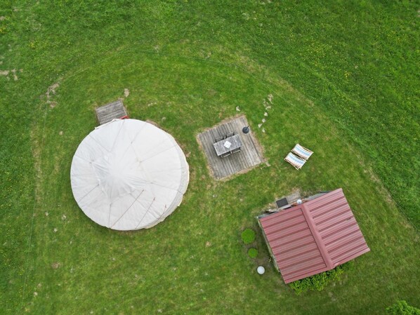 Vista aérea de una propiedad que incluye un gran silo blanco, una pequeña terraza de madera con una mesa y sillas, y un edificio con techo rojo.