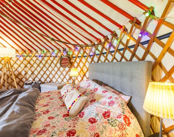 A cozy interior of a yurt with a bed, a headboard, and string lights. - Yurt Stay with Terrace and Panoramic Views in Denneville (Denneville)