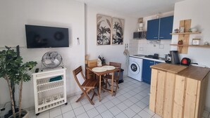 Une cuisine compacte équipée d’un lave-linge, d’une table à manger avec des chaises, d’un téléviseur fixé au mur et d’un ventilateur de plafond.