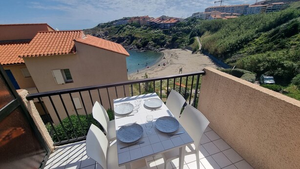 Un balcon avec une table et des chaises, donnant sur une plage et des immeubles.