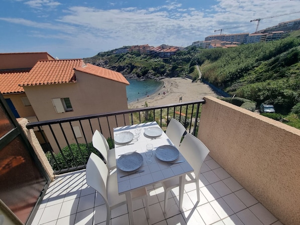 Ein Balkon mit Tisch und Stühlen, der Blick auf einen Strand und Gebäude gerichtet ist.