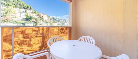 A balcony with a white table and four chairs, overlooking a hillside with buildings.