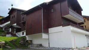 A multi-story building with a brown exterior and white lower section, featuring a staircase leading to the upper floors. - Les Gets: Charmant 2P+Coin Montagne, 5 Pers, Garage, Proche Centre et Pistes (Les Gets)