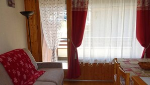 A cozy room with a sofa, a wooden dining table with chairs, and a window with curtains. - Les Gets: Charmant 2P+Coin Montagne, 5 Pers, Garage, Proche Centre et Pistes (Les Gets)