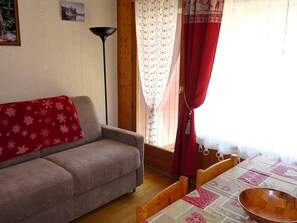A cozy living room with a sofa, a wooden dining table, and a red curtain.