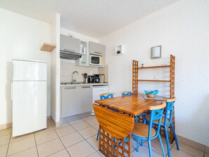 Una cocina compacta con un refrigerador blanco, un microondas y una cafetera. Hay una mesa de comedor de madera con sillas azules.