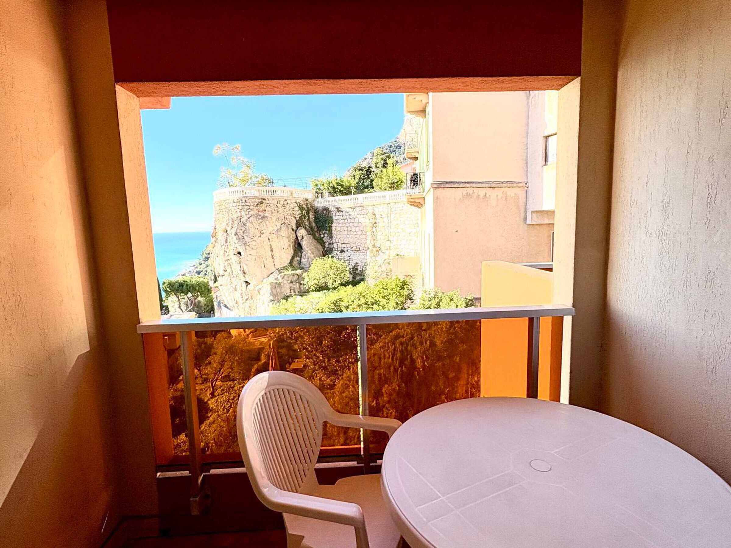 Un balcon avec une table et une chaise, donnant sur une falaise rocheuse et un immeuble.