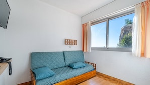 A room with a wooden sofa, a small wooden table, a telephone, and a window with curtains.