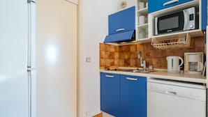 A compact kitchen with a white refrigerator, blue cabinets, a microwave, a coffee maker, and a dishwasher.