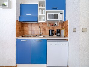 A compact kitchen with blue cabinets, a white microwave, a coffee maker, and a dishwasher. - Studio for 4, sea view, Wi-Fi included (Roquebrune-Cap-Martin)