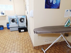 A laundry area with two washing machines, an ironing board, and a drying rack.