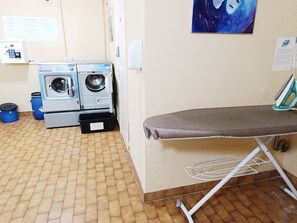 A laundry room with two washing machines, an ironing board, and a tiled floor. - Studio for 4, sea view balcony, Wi-Fi included (Roquebrune-Cap-Martin)