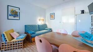 A cozy room with a wooden dining table, a blue sofa, and a wooden chair with a cut-out backrest. - Studio for 4, sea view balcony, Wi-Fi included (Roquebrune-Cap-Martin)