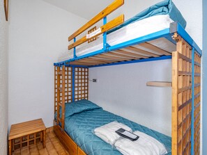 A bunk bed with a wooden frame and blue accents, a small wooden table, and a white pillow with a black object on it.