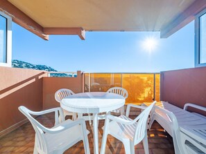 A balcony with a round table and white plastic chairs, a sofa, and a view of the sky and trees.