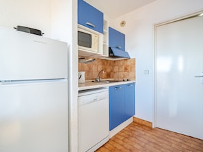 A compact kitchen with a white refrigerator, a microwave, and blue cabinets.