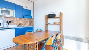 A compact kitchen with blue cabinets, a wooden dining table, and a built-in shelf unit.