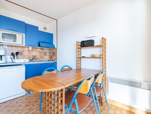 A compact kitchen with blue cabinets, a wooden dining table, and a built-in shelf unit.