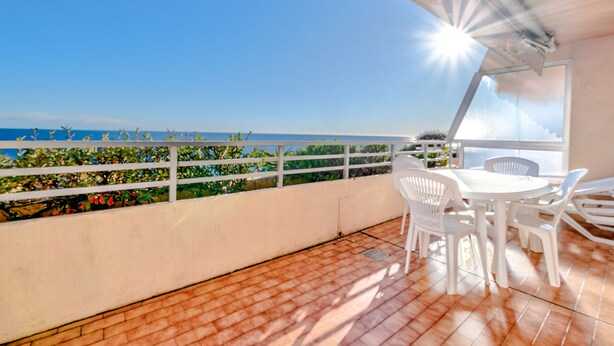 A terrace with a view of the sea, white chairs, and a table.