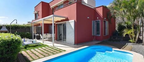 Una casa moderna de dos plantas con piscina, un porche cubierto y jardín.