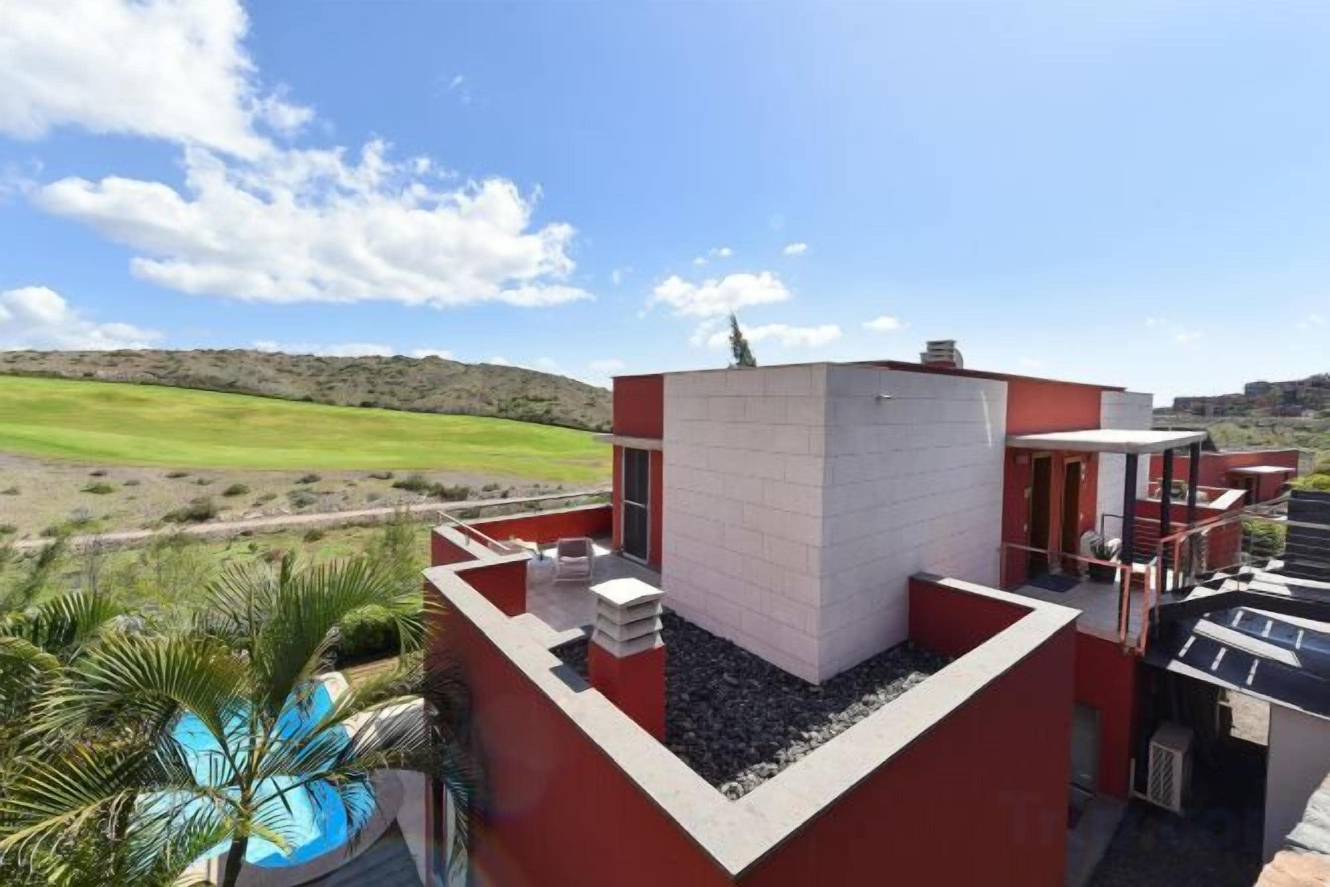 A modern building with a rooftop pool, red and white exterior, and a view of a green landscape.