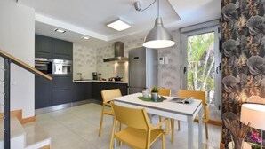 A modern kitchen with dark cabinets, a stainless steel range hood, and a dining area with a white table and yellow chairs.