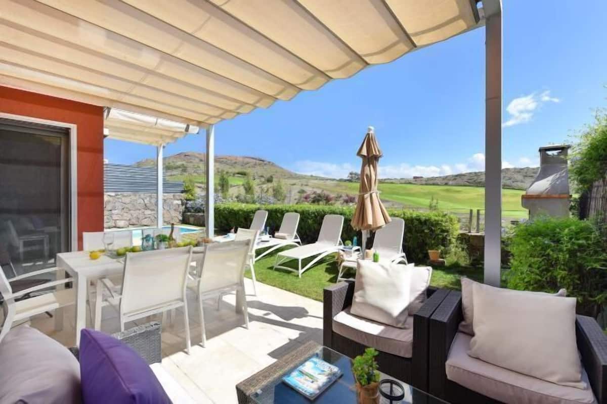 A covered patio with outdoor seating, a table, and a view of a golf course.