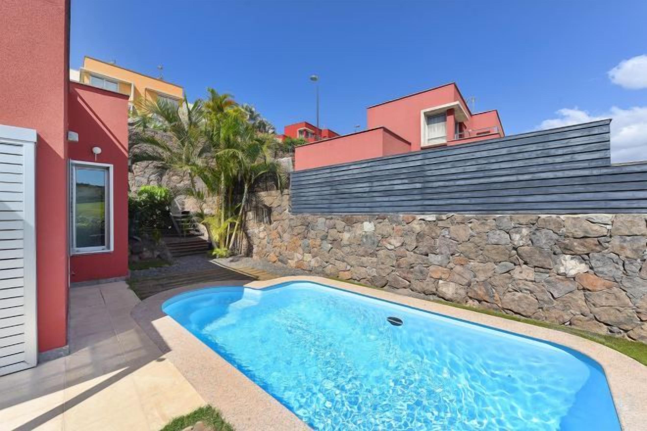 A swimming pool with a stone wall and a red building in the background.