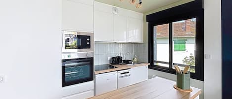 Cocina pequeña con armarios blancos, encimera de madera, horno empotrado y ventana con vistas a la calle.