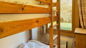 A bunk bed with a wooden frame and white bedding, a window with curtains, and a radiator below.