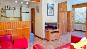 A cozy room with a wooden ceiling, a television, a red sofa, and a wooden cabinet.
