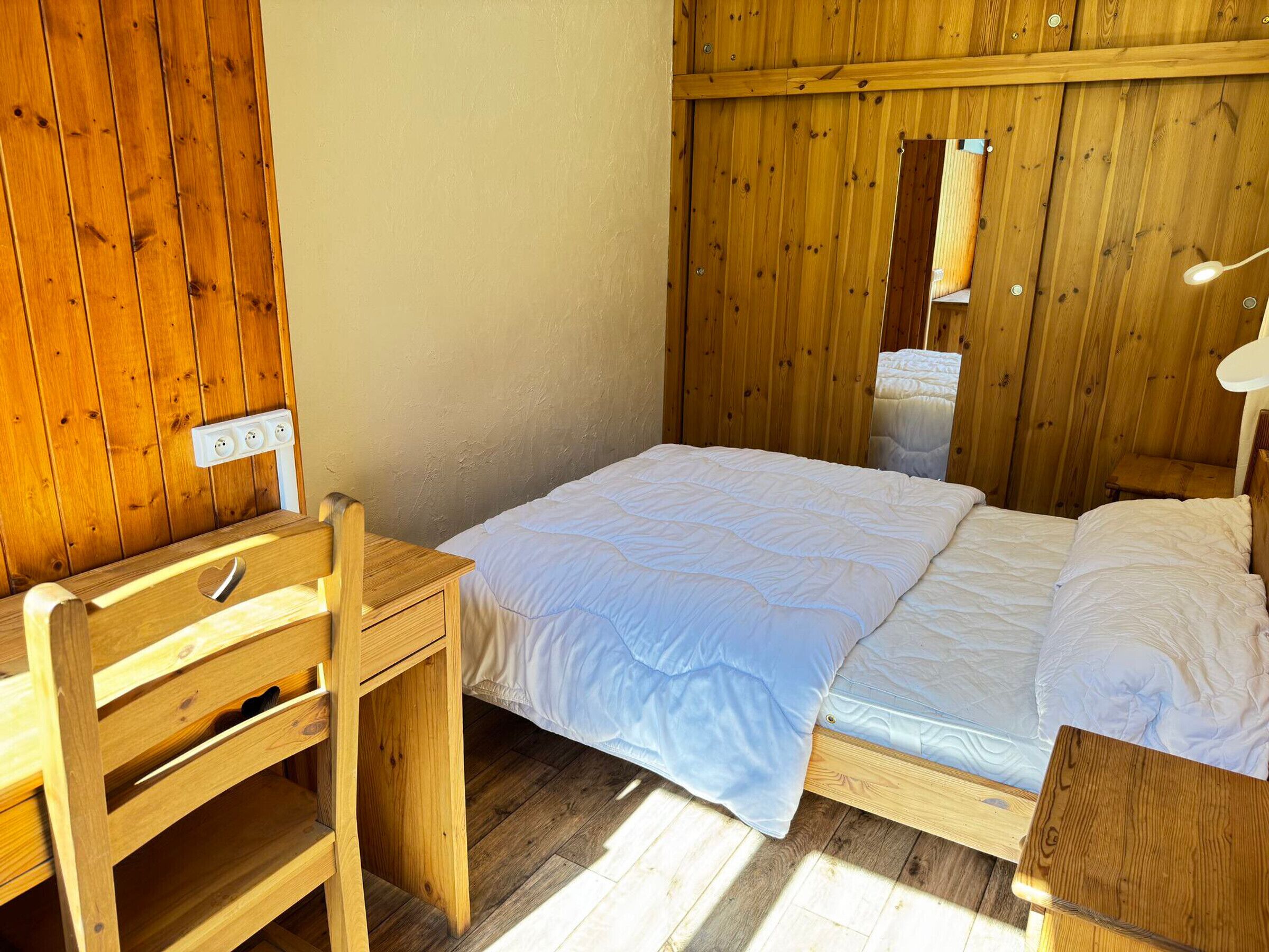 Een houten kamer met een bed, een bureau en een stoel.