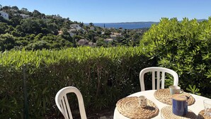 A table with chairs and woven placemats, overlooking a coastal landscape with houses and greenery.