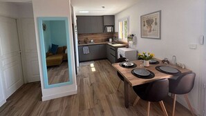 A compact living space with a kitchenette, a dining area with a table and chairs, and a living room with a sofa and a blue accent wall.