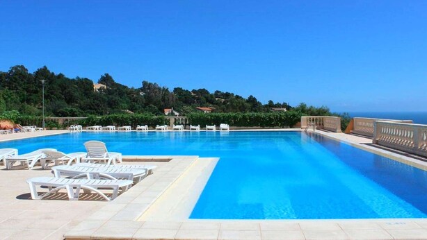 A rectangular swimming pool with clear blue water, surrounded by white lounge chairs and a tiled deck.