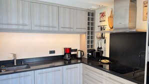 A modern kitchen with light wood cabinets, a black countertop, and stainless steel appliances.