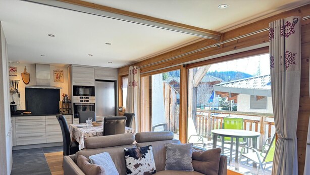 A cozy living room with a sofa, a dining table, and a kitchen in the background.
