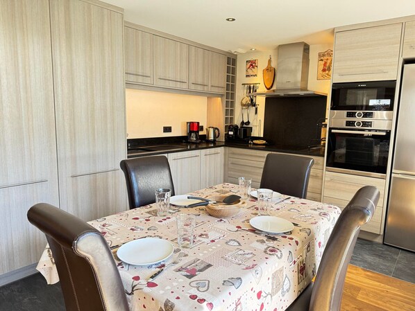 Una cocina moderna con armarios de madera clara, horno de acero inoxidable y una mesa de comedor con platos y vasos.