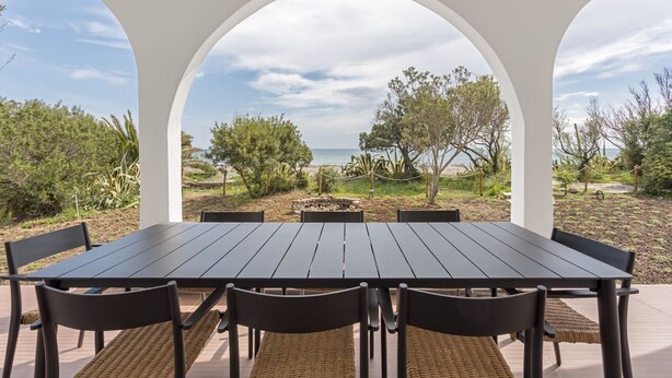 A table with six chairs and a bench, set in a covered outdoor area with white arches. - Villa Toschi beach front (TERTENIA)