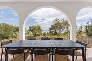 A table with six chairs and a bench, set in a covered outdoor area with white arches.