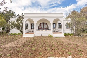 A white building with three arches and a central window, surrounded by a landscaped garden.