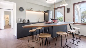 A modern kitchen with a central island, bar stools, pendant lighting, and a view of the outdoors. - Villa Toschi beach front (TERTENIA)