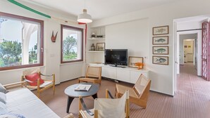A modern living room with a TV, wooden furniture, and a large window. - Villa Toschi beach front (TERTENIA)