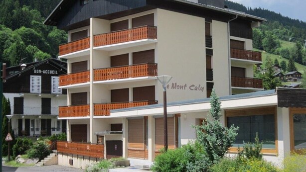 A multi-story hotel with balconies, a sign reading "Bon Accueil," and a view of a mountainous landscape. - Les Gets: Duplex Apartment 3 Rooms 7 People, Wifi, Garage (Les Gets)