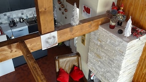 A kitchen with a wooden beam structure, a dining area with a red chair, and a fireplace with decorative items. - Les Gets: Duplex Apartment 3 Rooms 7 People, Wifi, Garage (Les Gets)