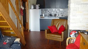 A cozy living room with a brown leather chair, a wooden staircase, and a kitchen area with grey cabinets and a microwave. - Les Gets: Duplex Apartment 3 Rooms 7 People, Wifi, Garage (Les Gets)