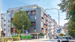 Ein modernes, mehrstöckiges Gebäude mit Balkonen, einer Fußgängerampel und einer begrünten Fassade.