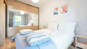 Ein modernes Schlafzimmer mit einem großen Spiegel, einem Bett mit gestreifter Bettwäsche und zwei abstrakten Wandbildern.